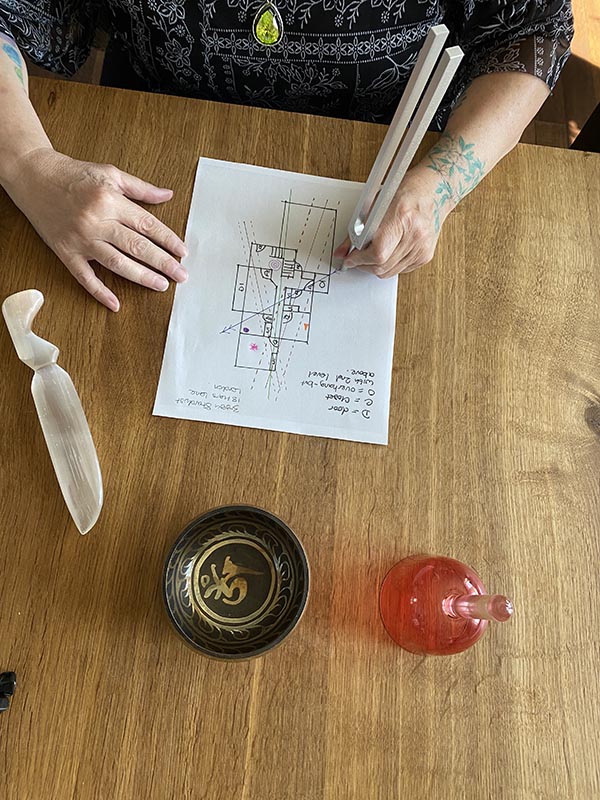 Photo: Zoe sitting at a table, using a tuning fork over a house floor plan
